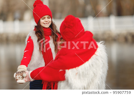 Mother and child in knitted winter hats on family Christmas vacation. Handmade wool hat and scarf for mom and kid. Knitting for kids. Knit outerwear. Woman and little girl in a park. 95907759