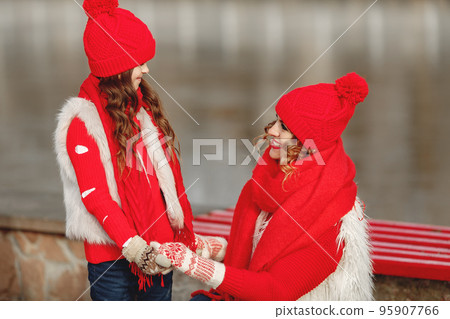 Mother and child in knitted winter hats on family Christmas vacation. Handmade wool hat and scarf for mom and kid. Knitting for kids. Knit outerwear. Woman and little girl in a park. Mother and child in knitted winter hats on family Christmas vacation. Handmade wool hat and scarf for mom and kid. Knitting for kids. Knit outerwear. Woman and little girl in a park. 95907766