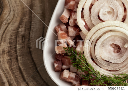 Italian pancetta, bacon cubes, diced ham, cutted pork, sliced onion in square white plate on wooden textured surface. Italian pancetta, bacon cubes, diced ham, cutted pork, sliced onion in square white plate on wooden textured surface. 95908681