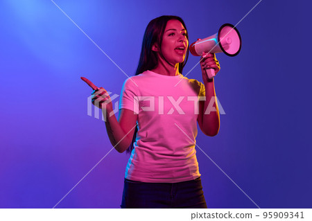 Portrait of young charming girl, student with megaphone on color background in neon light. Concept of beauty, art, fashion, human emotions and facial expressions 95909341
