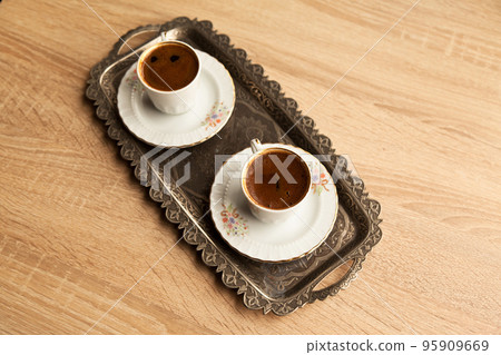 Traditional Turkish coffee in a patterned white cup in a metal tray on an oak coffee table 95909669