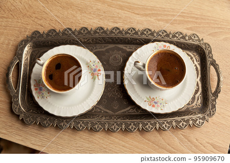 Traditional Turkish coffee in a patterned white cup in a metal tray on an oak coffee table 95909670