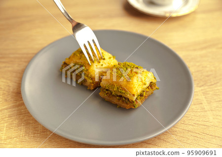 Baklava with pistachio, one of the most beautiful desserts of Turkish cuisine, in gray plate, on oak cutting board 95909691