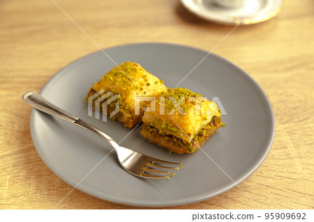 Baklava with pistachio, one of the most beautiful desserts of Turkish cuisine, in gray plate, on oak cutting board 95909692