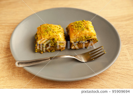 Baklava with pistachio, one of the most beautiful desserts of Turkish cuisine, in gray plate, on oak cutting board 95909694