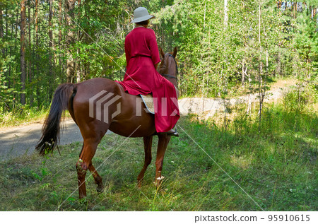 Woman in red dress rides a horse in early spring 95910615