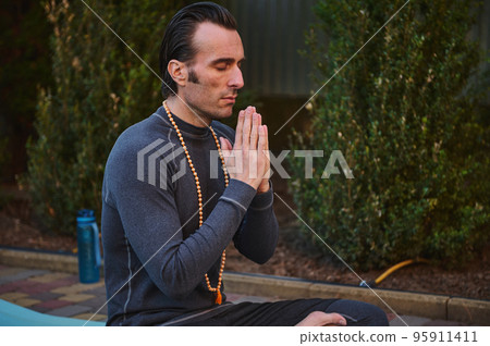 Close-up portrait of peaceful man yogi practicing yoga outdoors, meditating, putting palms together. Meditation. Yoga practice. Mindfulness. Prayer and gratitude. Spiritual growth. Health. Body care Close-up portrait of peaceful man yogi practicing yoga outdoors, meditating, putting palms together. Meditation. Yoga practice. Mindfulness. Prayer and gratitude. Spiritual growth. Health. Body care 95911411