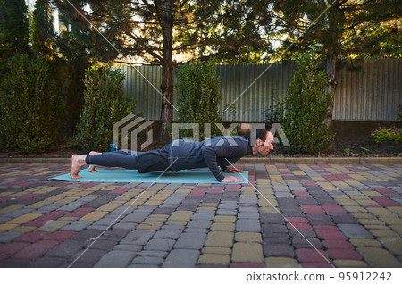Side portrait of an active athlete Caucasian man yogi in his 40s, doing Yoga chaturanga push-ups on a fitness mat while practicing outdoors. Sport Fitness workout. Active and healthy lifestyle 95912242