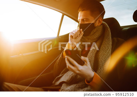 Young man in protective sterile mask in taxi car on a back seat checking her cell phone. Young man in protective sterile mask in taxi car on a back seat checking her cell phone. 95912510
