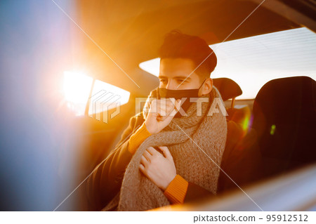Young man in protective sterile mask in taxi car on a back seat checking her cell phone. 95912512