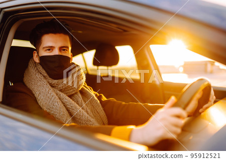 Young man in protective sterile medical mask driving car in quarantine city. Covid -19. Young man in protective sterile medical mask driving car in quarantine city. Covid -19. 95912521