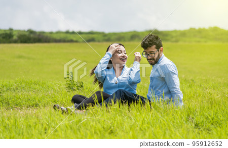 A couple in love sitting in the field, Romantic couple sitting on the grass outdoors, Smiling teenage couple sitting on the grass on a sunny day 95912652