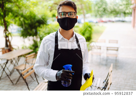 Disinfecting to prevent COVID-19. Waiter in protective face mask and gloves cleaning. Disinfecting to prevent COVID-19. Waiter in protective face mask and gloves cleaning. 95912837