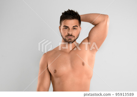 Young man showing hairless armpit after epilation procedure on light grey background 95913589