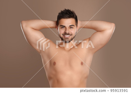 Young man showing hairless armpits after epilation procedure on brown background 95913591
