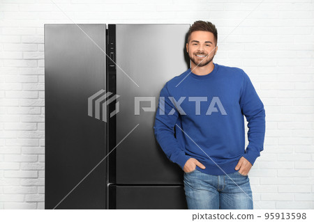 Happy young man near modern refrigerator indoors Happy young man near modern refrigerator indoors 95913598