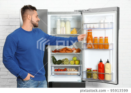 Young man taking juice out of refrigerator indoors Young man taking juice out of refrigerator indoors 95913599