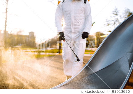 Man wearing protective suit disinfecting the playground in the sun with spray. Covid -19. Cleaning. 95913650