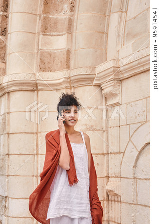 Positive dark haired woman walking through the street and chatting at her smartphone 95914541