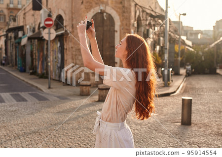 Ginger girl making photo of the ancient street or taking selfie outdoors 95914554