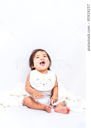 A baby girl sitting in front of a white background and laughing> 95919257