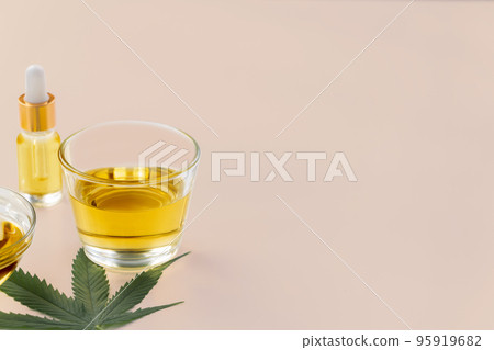 Glass bowl of legalized CBD oil, cannabis bud, and a hemp leaf on background. 95919682