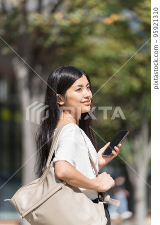 肩上背著背包的女商人拿著智能手機 肩上背著背包的女商人拿著智能手機 95921310