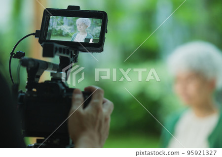 Photographer taking video of senior woman Photographer taking video of senior woman 95921327