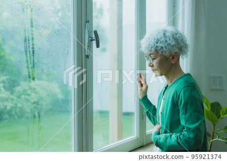 Senior woman by the window in the rain Senior woman by the window in the rain 95921374