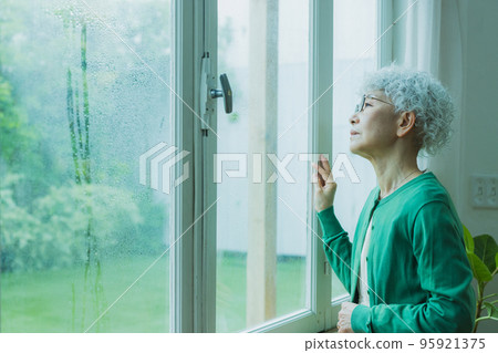 Senior woman by the window in the rain Senior woman by the window in the rain 95921375