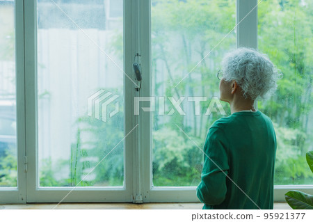 Senior woman by the window in the rain Senior woman by the window in the rain 95921377