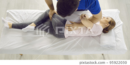 Male physiotherapist provides physical assistance to female patient with back and leg injuries. Male physiotherapist provides physical assistance to female patient with back and leg injuries. 95922030