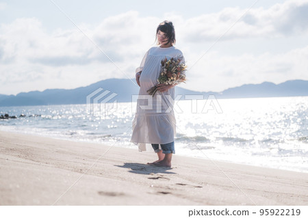Pregnant woman standing with a bouquet on the beach 95922219