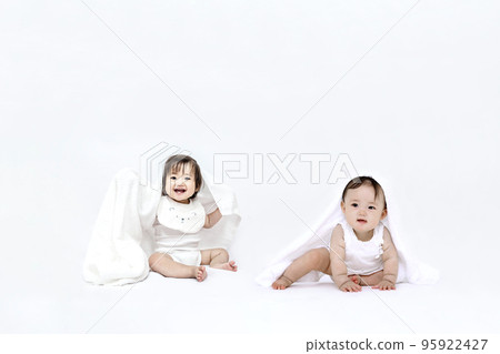 兩個女嬰坐在白色背景前玩浴巾 兩個女嬰坐在白色背景前玩浴巾 95922427