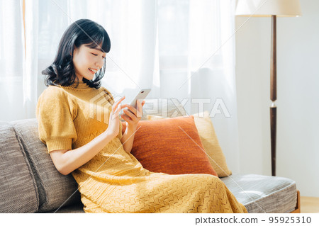 一個女人坐在沙發上使用智能手機 95925310
