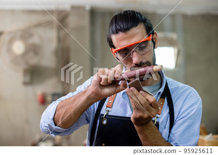 young carpenter man wearing goggles working using sandpaper for wood polishing. 95925611