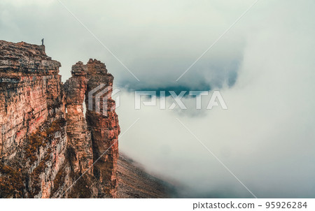 Awesome caucasus landscape with silhouette of hiker above white clouds and Rocks of Big Bermamyt - the so-called "Monks".  Man with backpack in high mountains. Panoramic view. 95926284