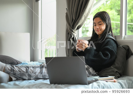 Carefree teenage girl watching video or browsing internet websites on laptop in her bedroom Carefree teenage girl watching video or browsing internet websites on laptop in her bedroom 95926693