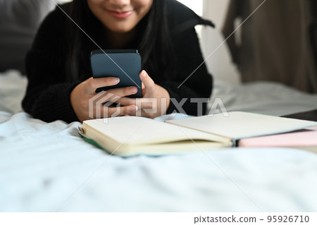 Teenage girl typing text message, chatting online on mobile phone while lying on bed 95926710