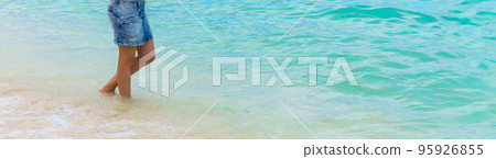 A young woman stands barefoot on the sandy seashore. 95926855