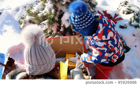 winter, frosty, snowy, sunny day. Happy family with small children unpack boxes with gifts under the Christmas tree, outdoors. High quality photo 95926986