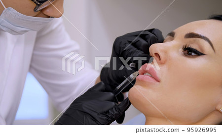 medical office, doctor in black sterile gloves, injecting hyaluronic acid into the patient lips. Procedure for increasing the volume of lips, correction of lips shape. High quality photo 95926995