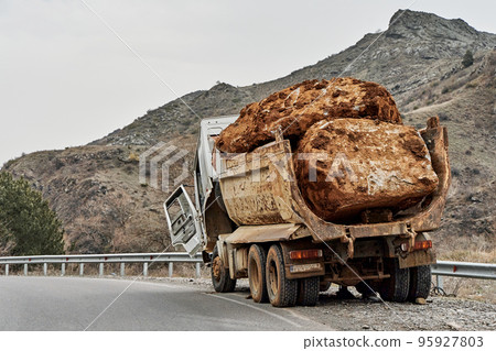 An old truck carrying a huge stone in the back broke down on a mountain road An old truck carrying a huge stone in the back broke down on a mountain road 95927803