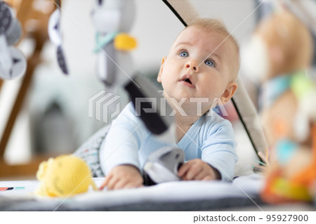 Cute baby boy playing with hanging toys arch on mat at home Baby activity and play center for early infant development. Baby playing at home Cute baby boy playing with hanging toys arch on mat at home Baby activity and play center for early infant development. Baby playing at home 95927900