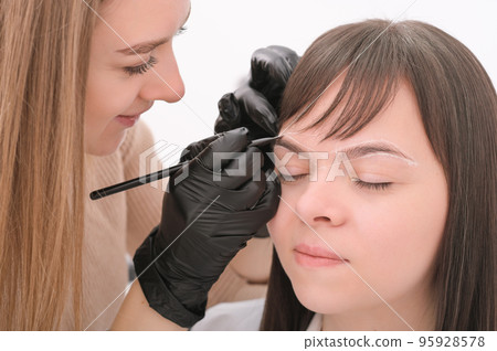Brow marking and measuring before microblading or henna tattoo close-up. White brow paste, threading. young beautician woman professional with client. Brow marking and measuring before microblading or henna tattoo close-up. White brow paste, threading. young beautician woman professional with client. 95928578