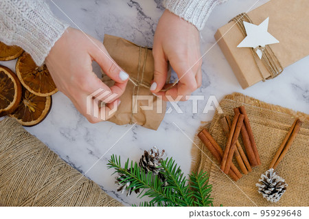 Woman making Box with New Year's gifts, wrapped in craft paper and decorated with cinnamon sticks. Holidays and Gifts concept. Handmade Eco friendly alternative green Christmas presents zero waste Top 95929648