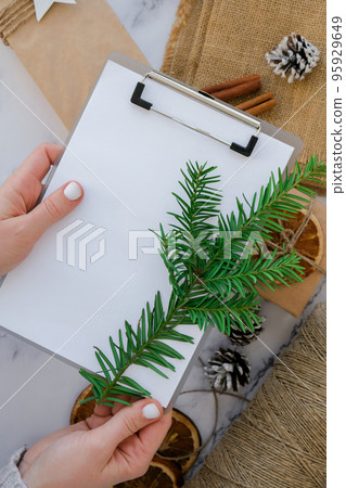 Woman preparing for christmas holidays. Writing gift list. Box with New Year's gifts, wrapped in craft paper and decorated with fir branch, dry orange slices, cinnamon sticks. Handmade Eco friendly Woman preparing for christmas holidays. Writing gift list. Box with New Year's gifts, wrapped in craft paper and decorated with fir branch, dry orange slices, cinnamon sticks. Handmade Eco friendly 95929649