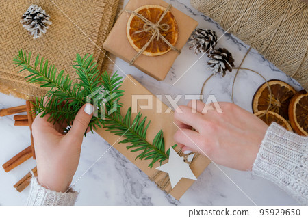 Woman making Box with New Year's gifts, wrapped in craft paper and decorated with fir branch. Holidays and Gifts concept. Handmade Eco friendly alternative green Christmas presents zero waste Top view Woman making Box with New Year's gifts, wrapped in craft paper and decorated with fir branch. Holidays and Gifts concept. Handmade Eco friendly alternative green Christmas presents zero waste Top view 95929650