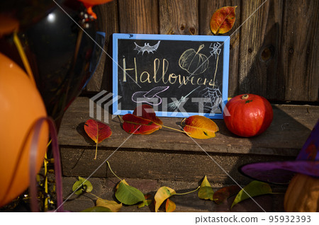 Close-up of a chalkboard with lettering Halloween, a pumpkin on the wooden doorstep with dry autumn fallen leaves 95932393