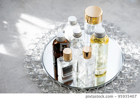 Various cosmetic bottles arranged on a mirrored tray shimmering in the morning light Various cosmetic bottles arranged on a mirrored tray shimmering in the morning light 95935407
